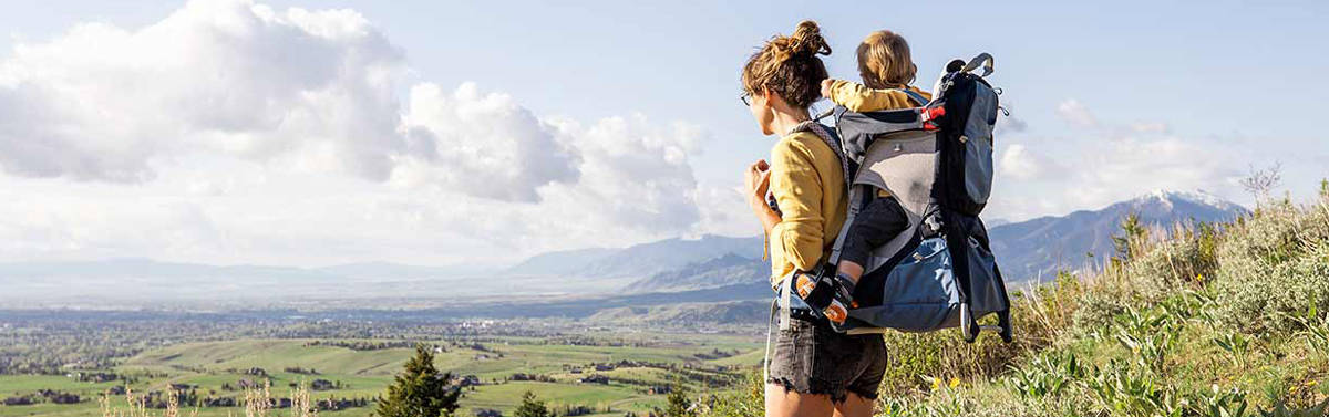 Woman with a child in a backpack carrier looking out over fields.