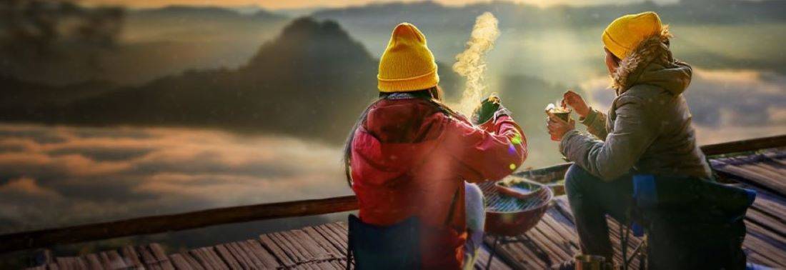 Women drinking coffee over campfire